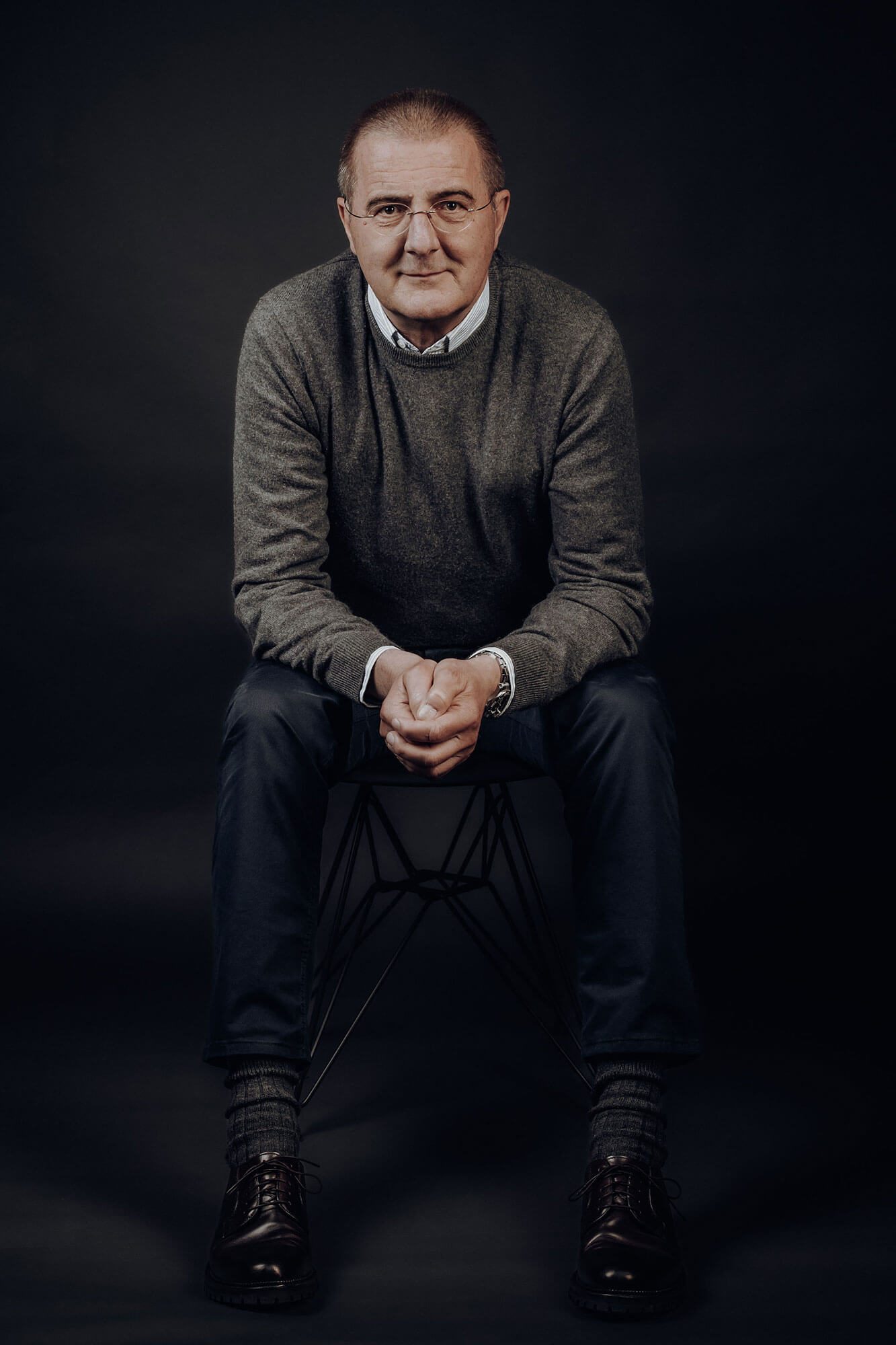 Geschäftsführer Jens Baldauf Der Geschäftsführer sitzt lächelnd auf einem Stuhl, trägt einen grauen Pullover und Jeans.